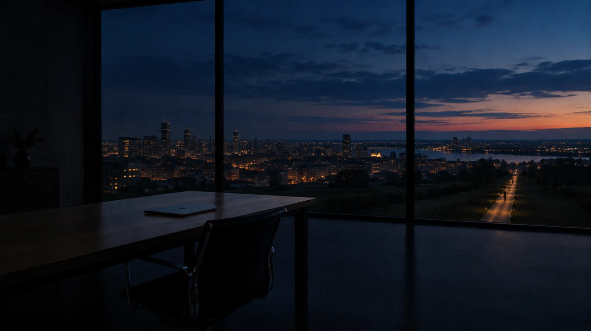 An empty office at night overlooking a city, one desk lamp still on
